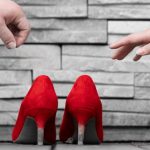 a pair of hands reaching for a pair of red high heels